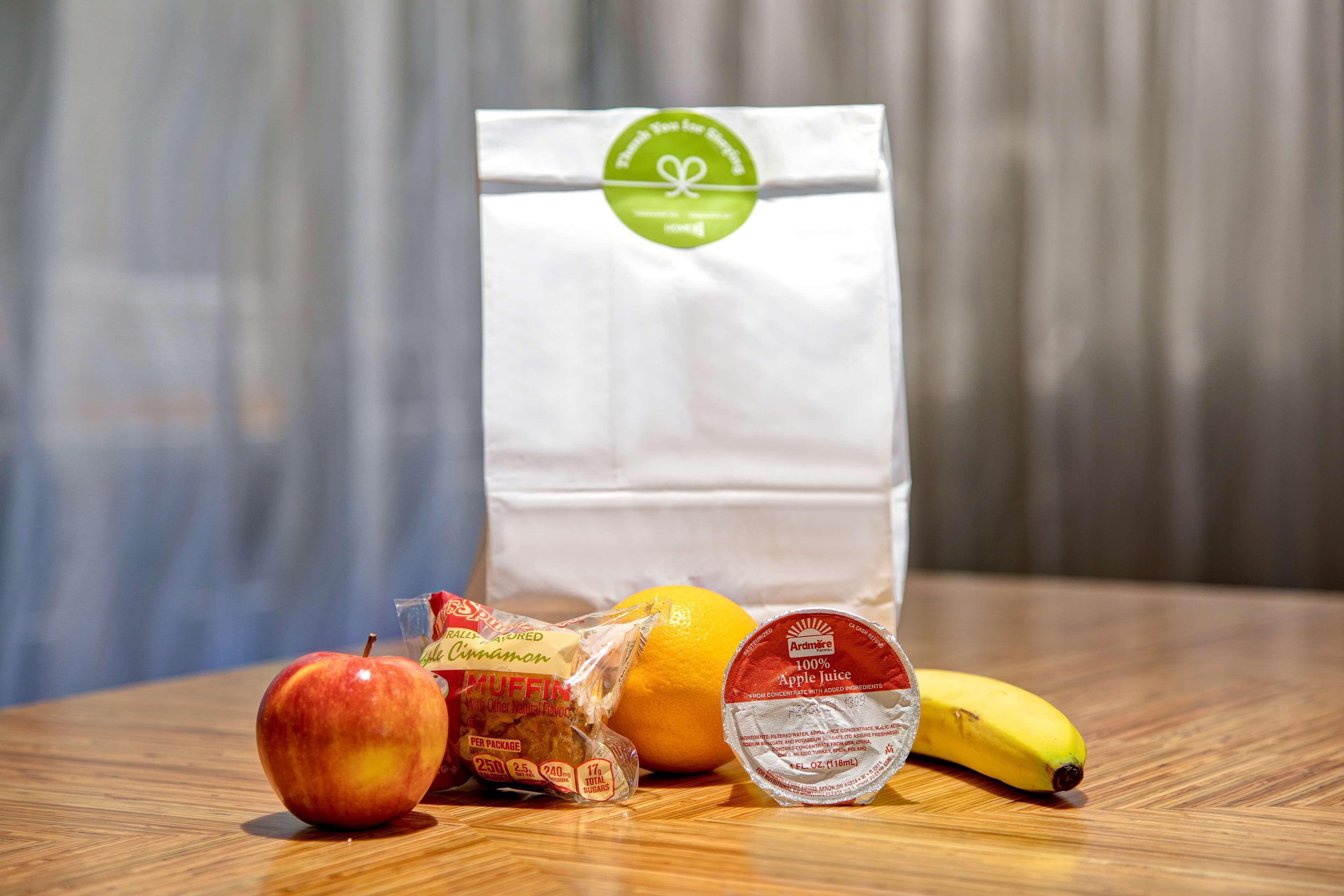A table with a bag of organic produce, an apple, a banana, a lemon, and a container of apple juice.