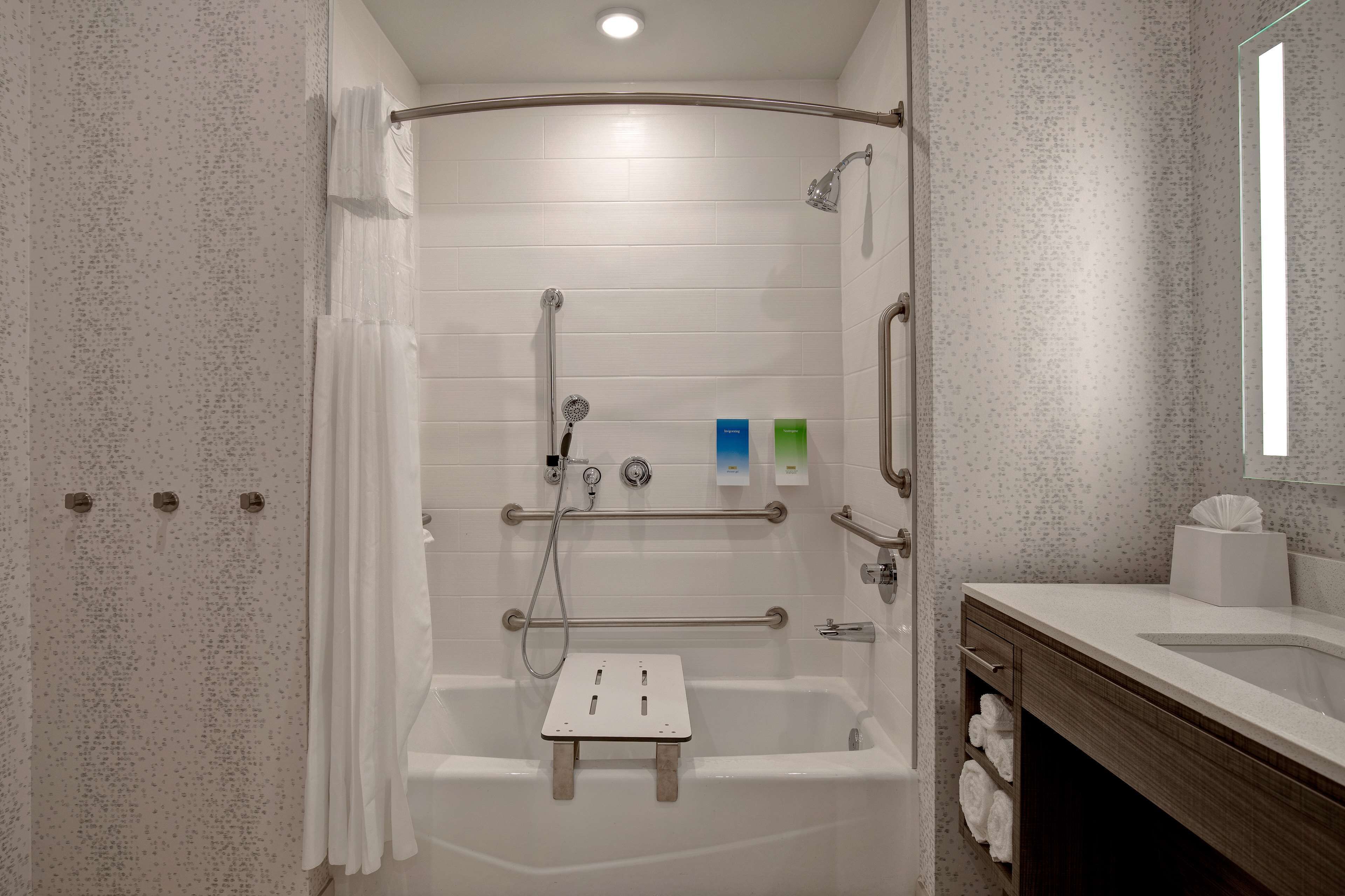 A modern bathroom with a walk-in shower, grab bars, a towel rack, and a vanity with a mirror.