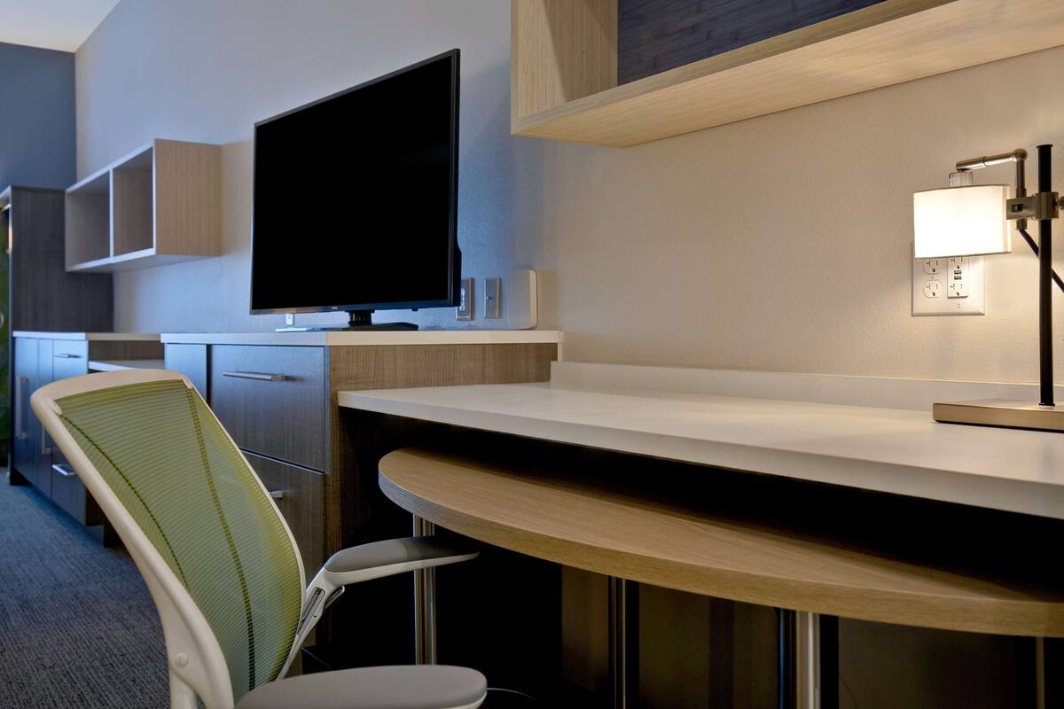 A modern hotel room with a flat-screen TV, a desk, a chair, and a lamp.