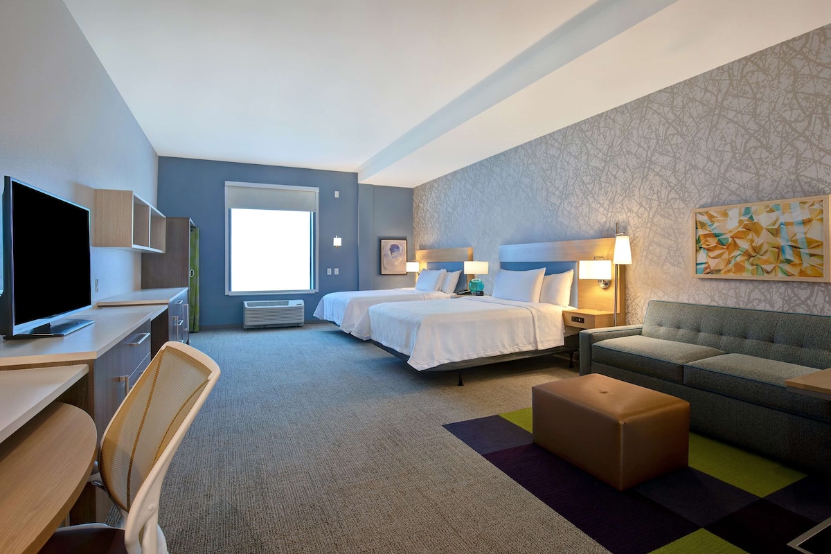 A hotel room with a bed, a sofa, a desk, a television, and a window.