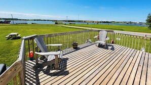 Une terrasse en bois avec des fauteuils Adirondack et une table de pique-nique, le tout donnant sur un lac.
