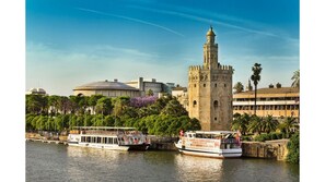 Une tour historique et un bâtiment moderne situés au bord d’une rivière, avec des bateaux amarrés à proximité.