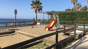 A beach playground with a slide, swings, and a fenced area.
