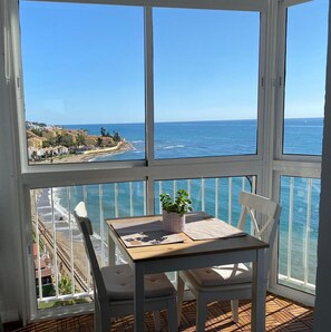Un balcon avec une table et des chaises, offrant une vue sur la côte, avec des bâtiments et la mer.