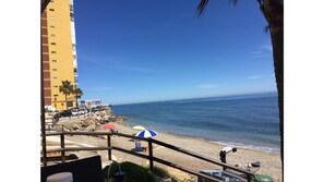 Une vue sur la plage, avec un bâtiment jaune, des palmiers et un ciel bleu dégagé.