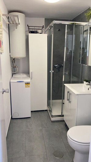 Une petite salle de bain comprenant des toilettes, un espace douche, un lave-linge et un lavabo.