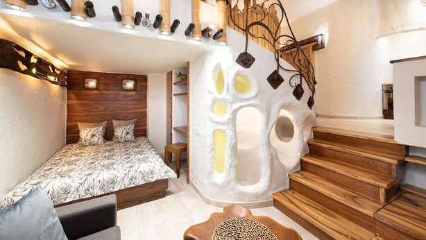 Un dormitorio con cama, cabecera de madera, una escultura de pared original y una escalera con barandilla de madera.