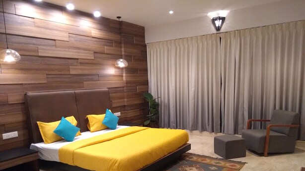A modern bedroom with a wooden headboard, a large bed with yellow bedding, a grey armchair, and a patterned rug.