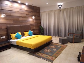 Un dormitorio moderno con cabecera de madera, una cama grande con ropa de cama amarilla, un sillón gris y una alfombra estampada.