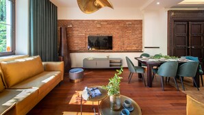 A modern living room with a brick wall, a flat-screen TV, a dining area with chairs, a sofa, and a coffee table. - Exotic Elegance - IR sauna, aircon, 3-bedrooms, 2 bathrooms, Wi-Fi (Krakow, malopolska)
