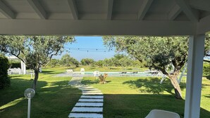 Un espacio exterior cubierto con un sendero de piedra que lleva a una piscina, rodeado de vegetación y mobiliario blanco para exteriores.