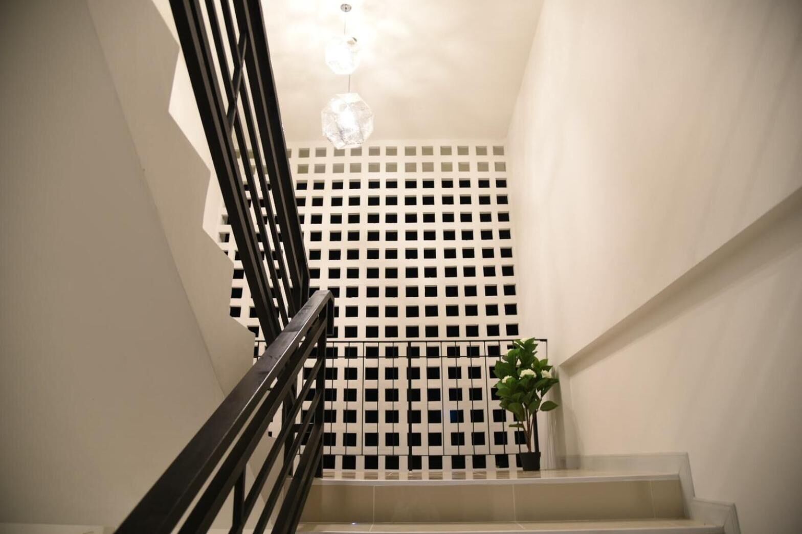 A staircase with a black railing, a white wall with a grid pattern, and a hanging light fixture.