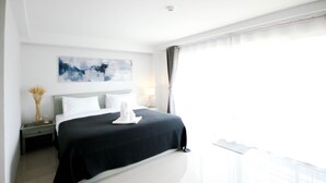 Habitación de hotel moderna con una cama grande, una mesita de noche, una lámpara y vistas al exterior.