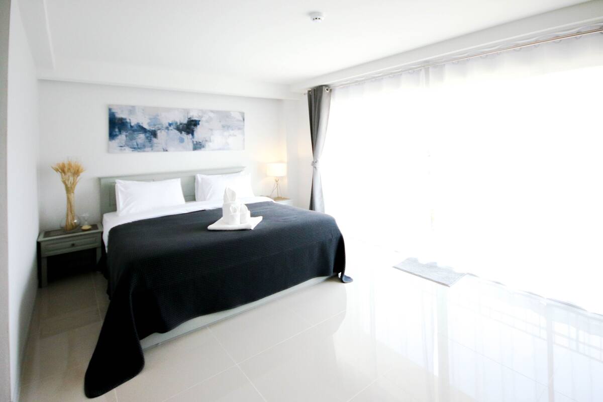 Ein modernes Hotelzimmer mit einem großen Bett, einem Nachttisch, einer Lampe und Blick ins Freie.