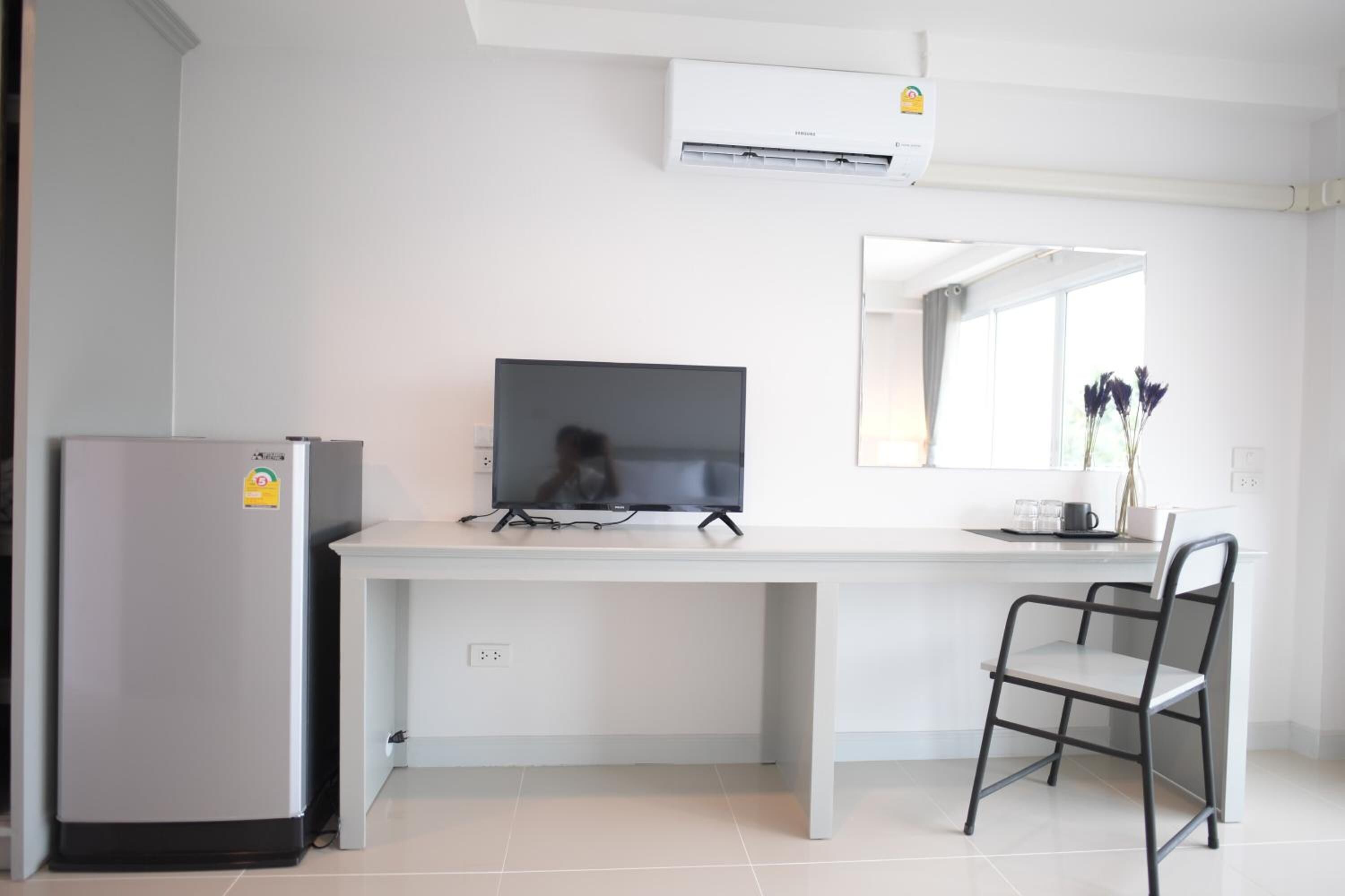 A modern kitchen with a refrigerator, a flat-screen TV, a white countertop, and a chair.