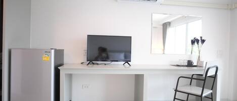 A modern kitchen with a refrigerator, a flat-screen TV, a white countertop, and a chair.