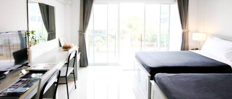 A hotel room with a bed, a desk with a computer, a TV, and a window with curtains.