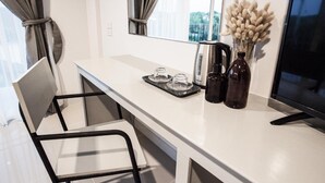Una habitación de hotel moderna con un escritorio blanco, una silla, un televisor de pantalla plana, una cafetera y un jarrón con flores secas.