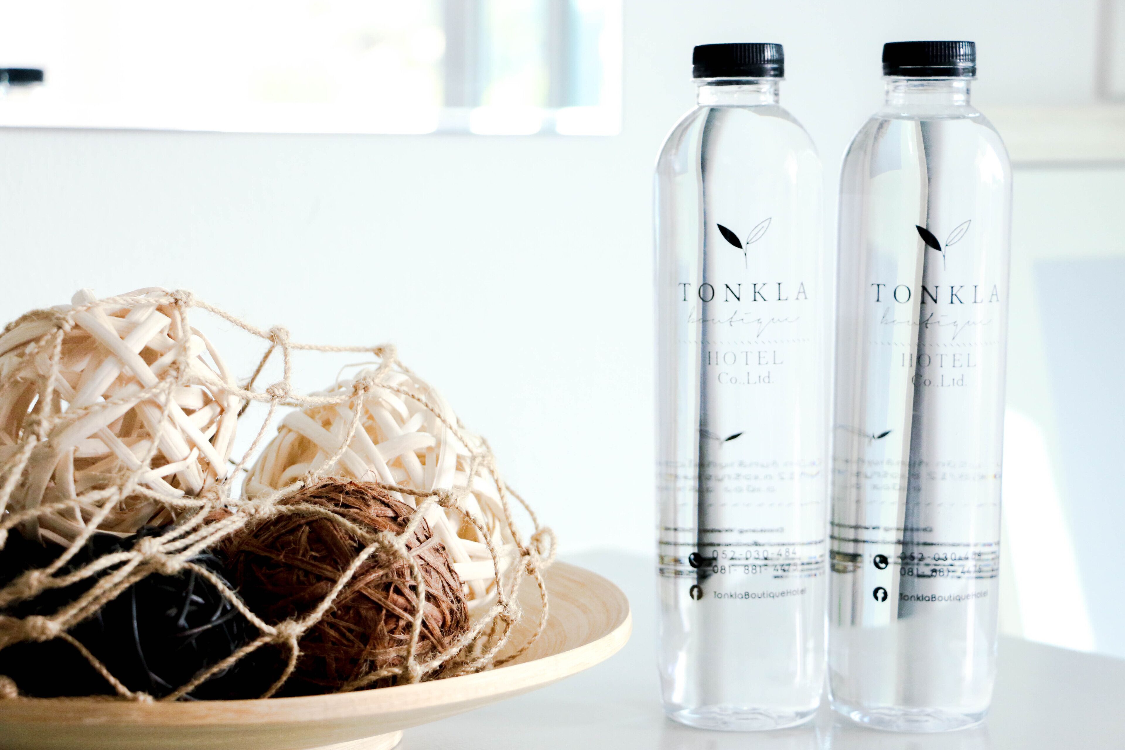 Two bottles of Tonka Hotel water on a table next to a wooden bowl with a straw ball.