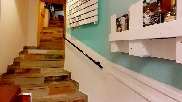 Una escalera de madera con escalones que conducen a una plataforma, un cartel fijado a la pared y un estante con botellas.
