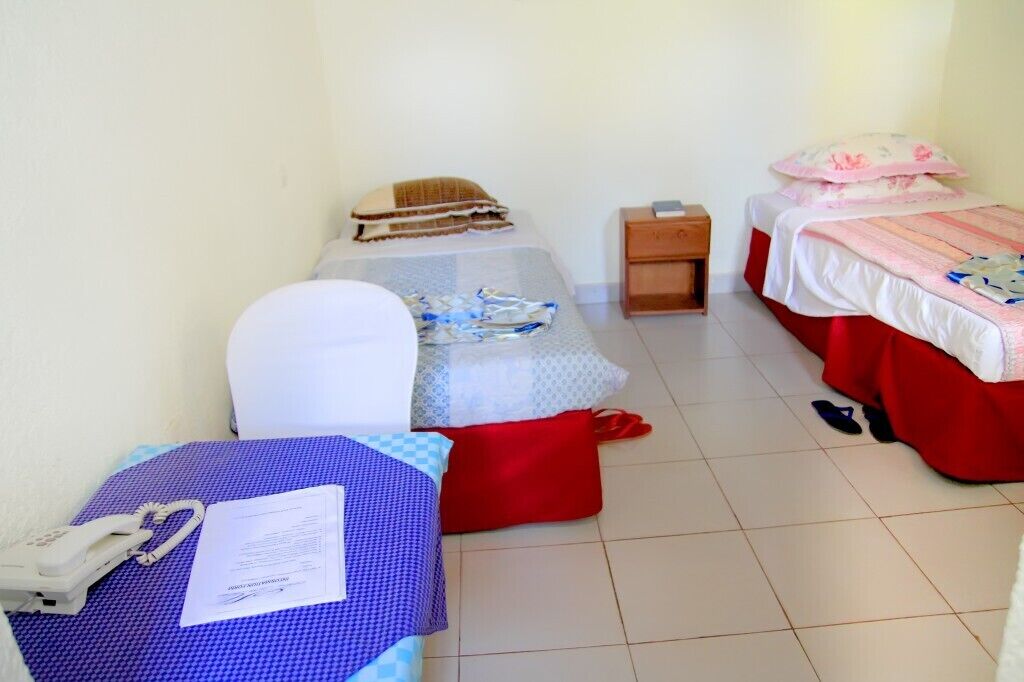 A small, compact room with two beds, a desk, and a chair. There is a telephone on the desk and a pair of shoes on the floor.