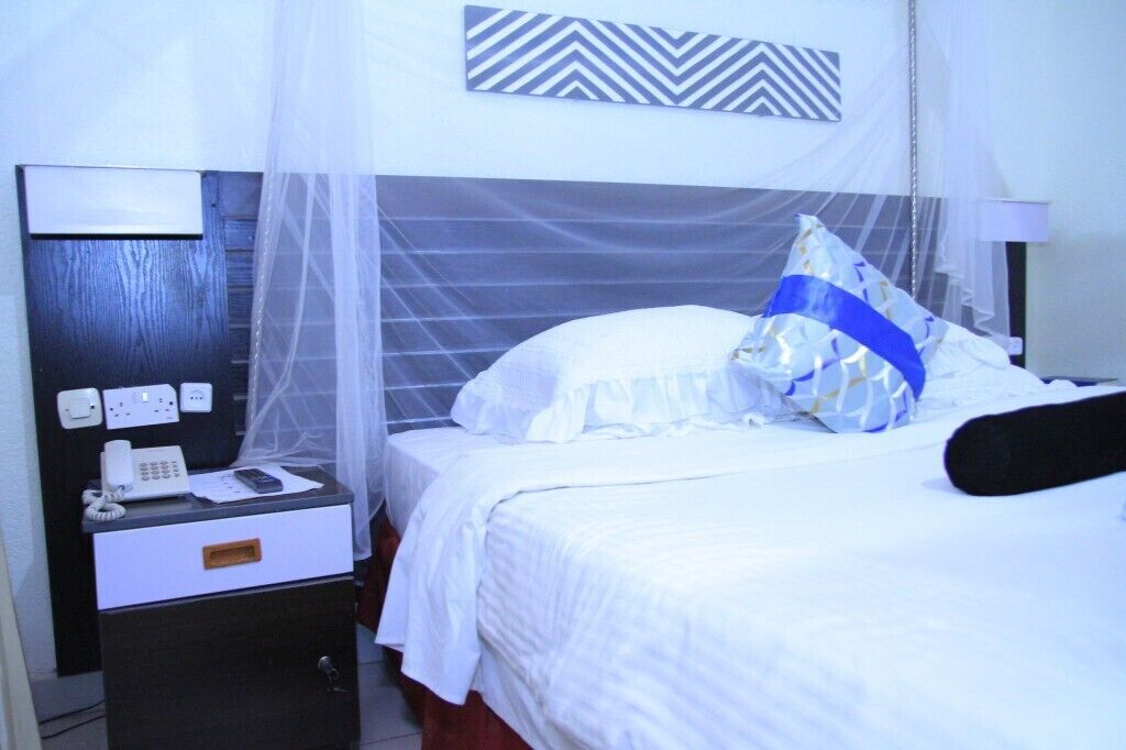 Une chambre d’hôtel avec un lit, une table de chevet avec un téléphone et une lampe, et un élément décoratif mural au-dessus du lit.