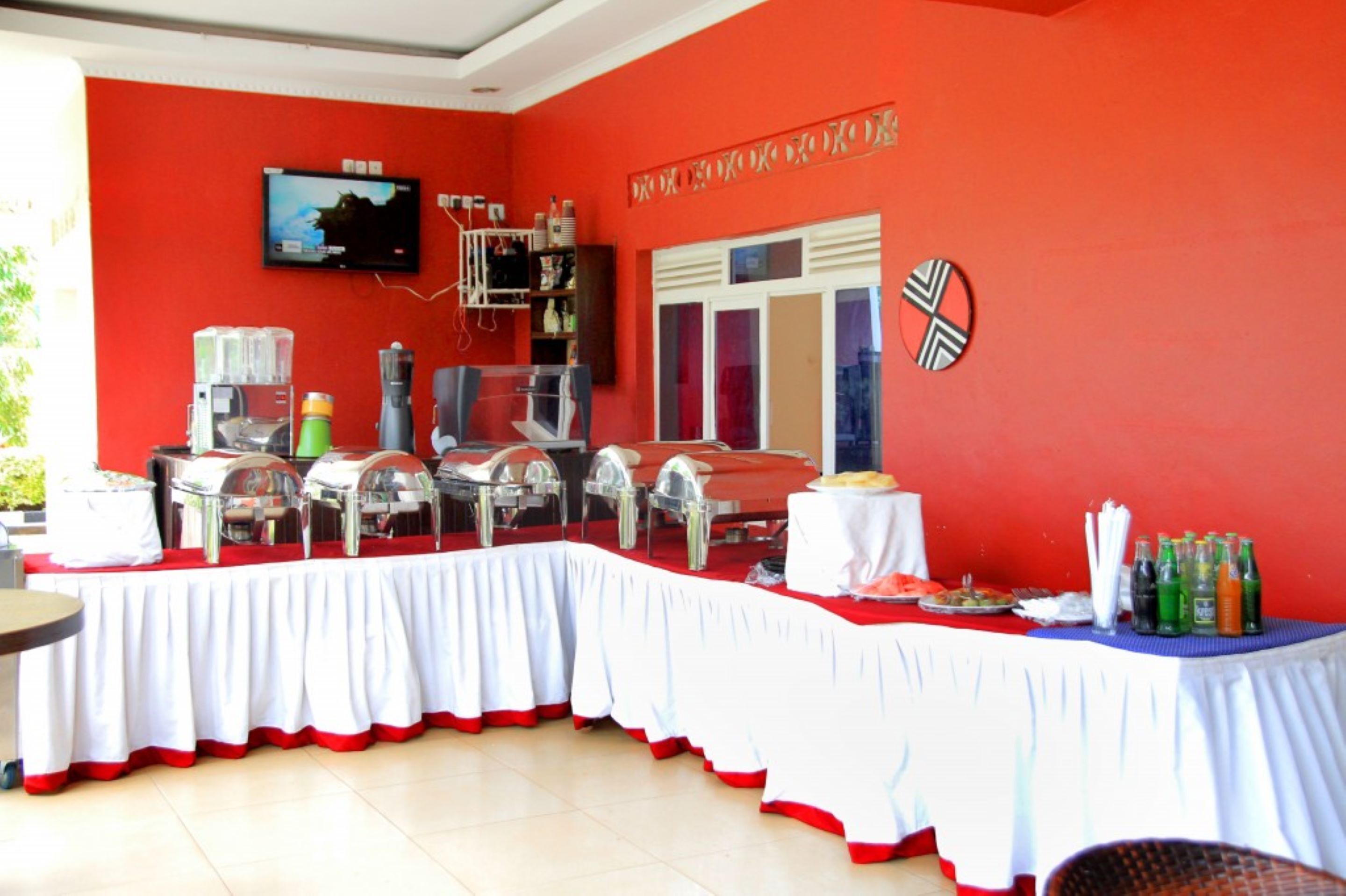 Un comedor con pared roja, televisor sobre una mesa de buffet y ventana con persianas.