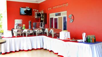 Un comedor con pared roja, televisor sobre una mesa de buffet y ventana con persianas.