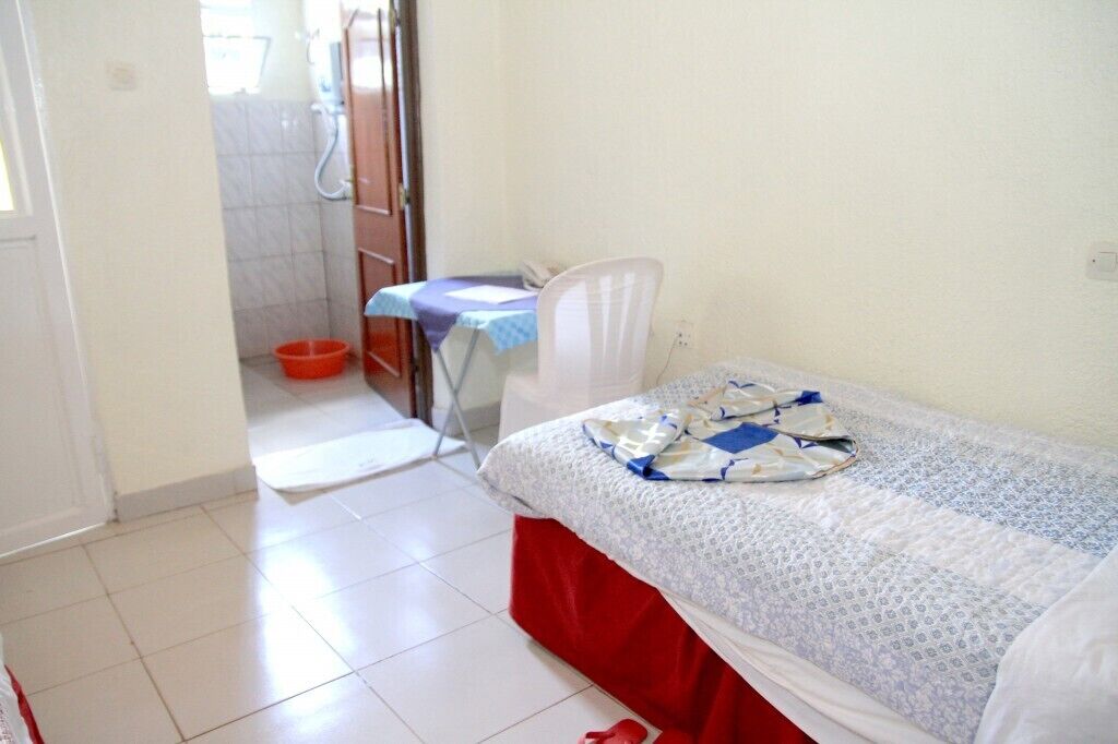 A small, clean room with a single bed, a chair, a table, and a shower area.