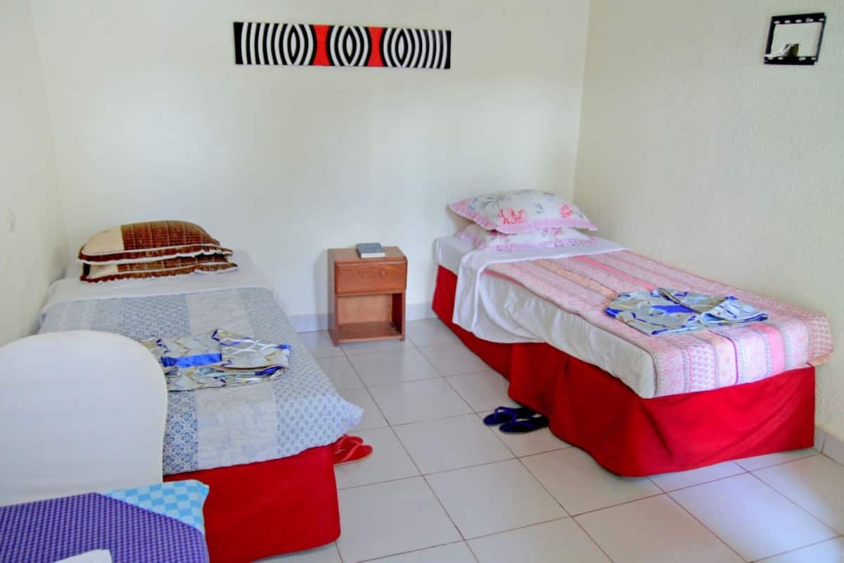 A room with two beds, a small wooden nightstand, and a wall-mounted light switch.