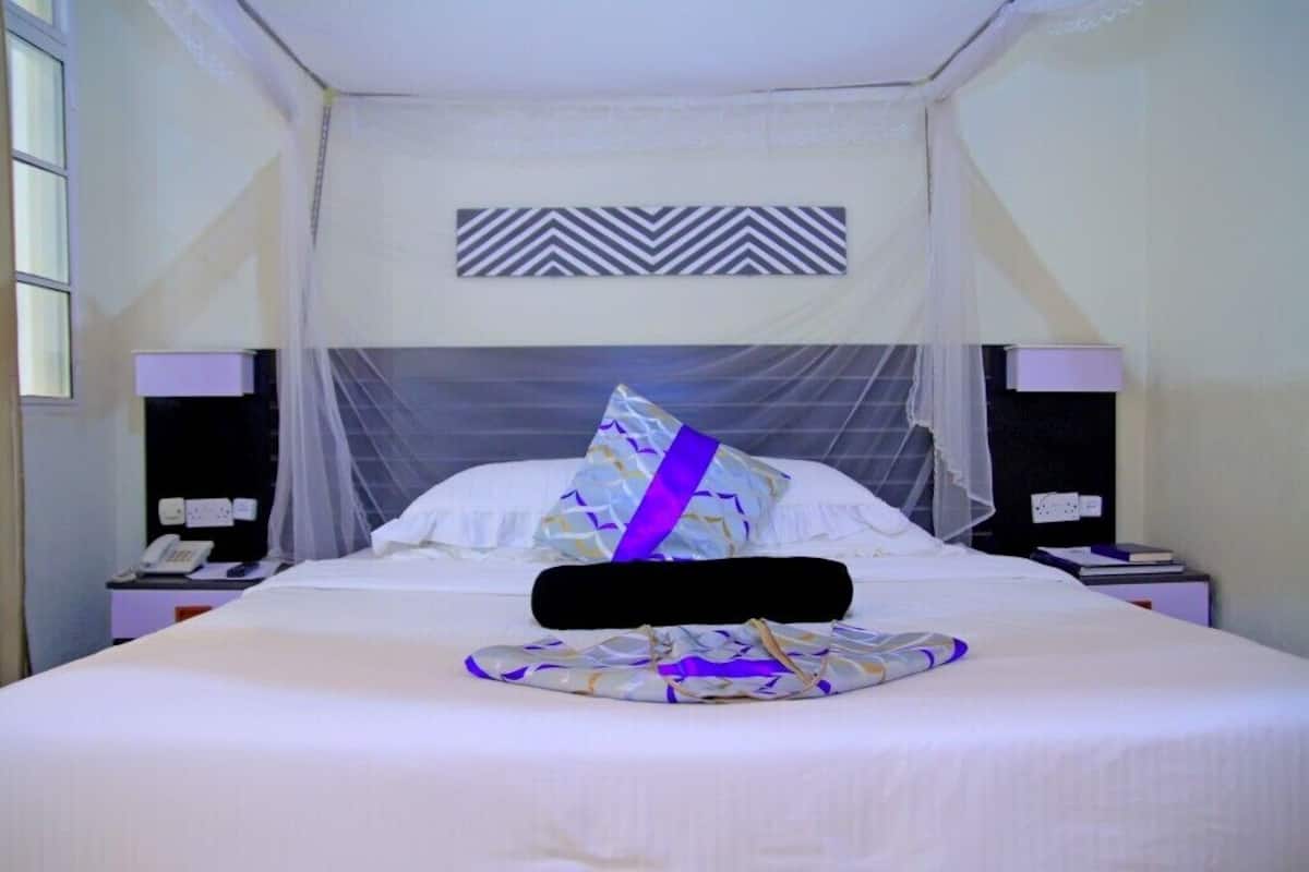 A hotel room with a bed, a nightstand, a telephone, and a wall-mounted decorative panel.