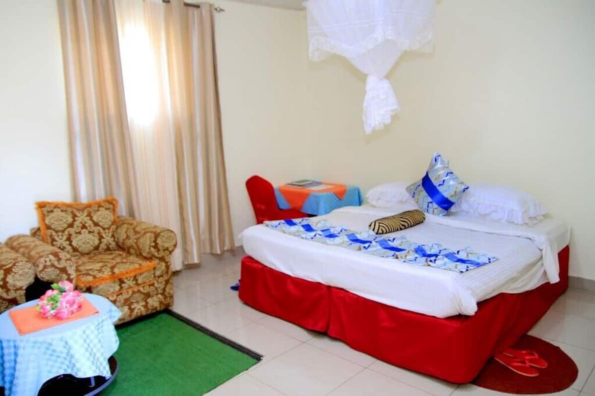 A hotel room with a bed, a sofa, a small table with a book, and a chair.