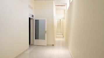 A narrow, well-lit hallway with a door at the end, tiled floor, and plain walls.