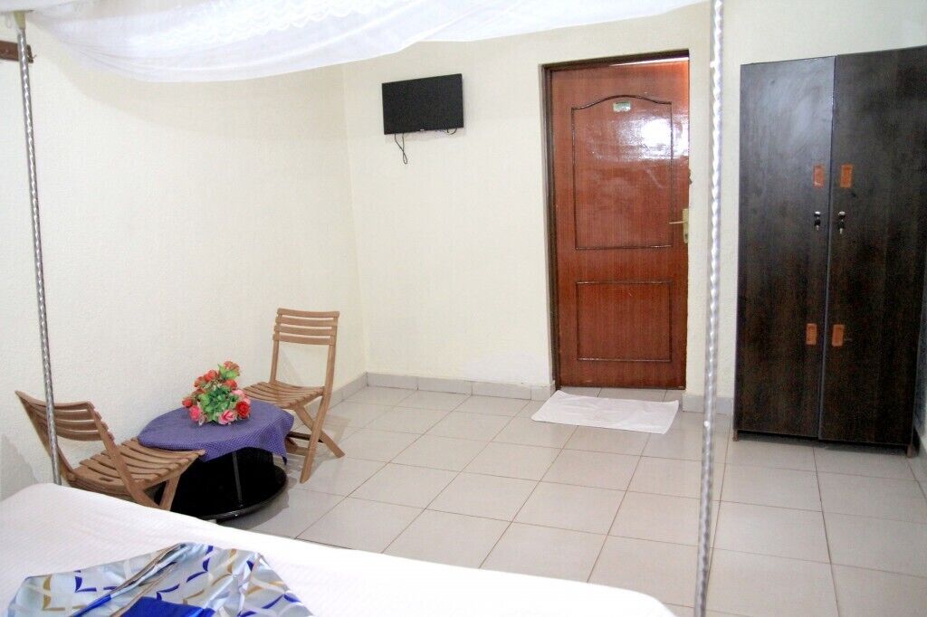 Una habitación con una cama, una mesita con sillas, una puerta de madera y un armario.