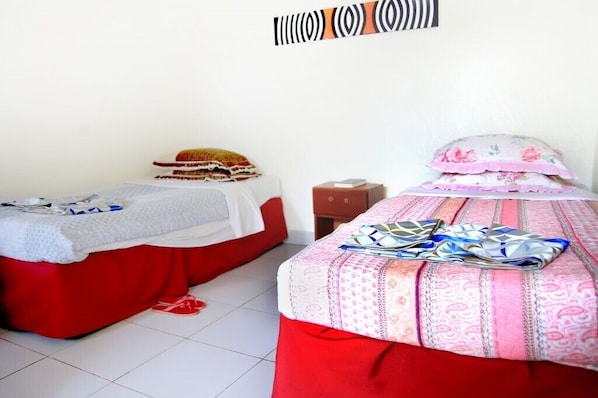 Two single beds with red bedding, a small wooden nightstand, and a wall decoration. - Silent Hill Hotel (Mukarange)