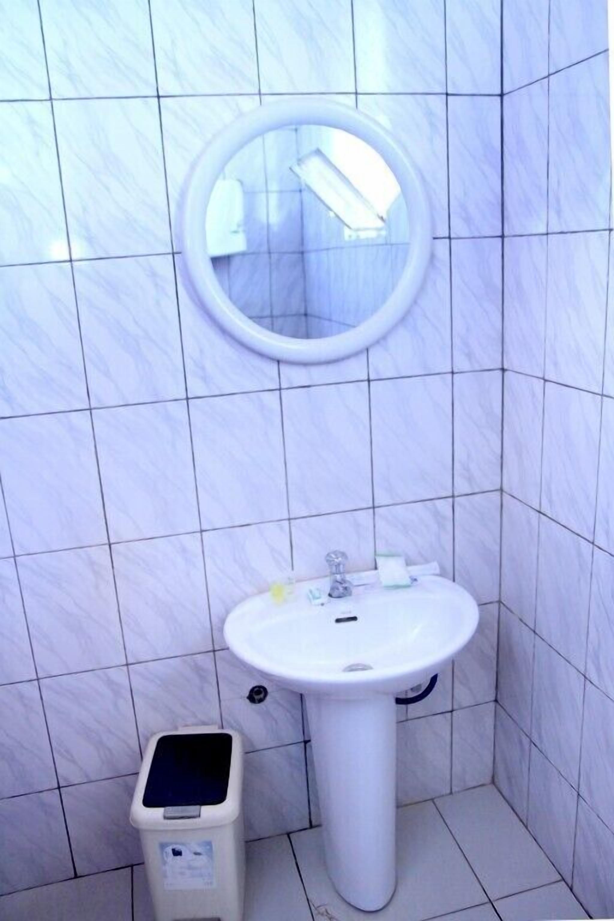 Un baño con lavamanos blanco, un espejo y un bote de basura.
