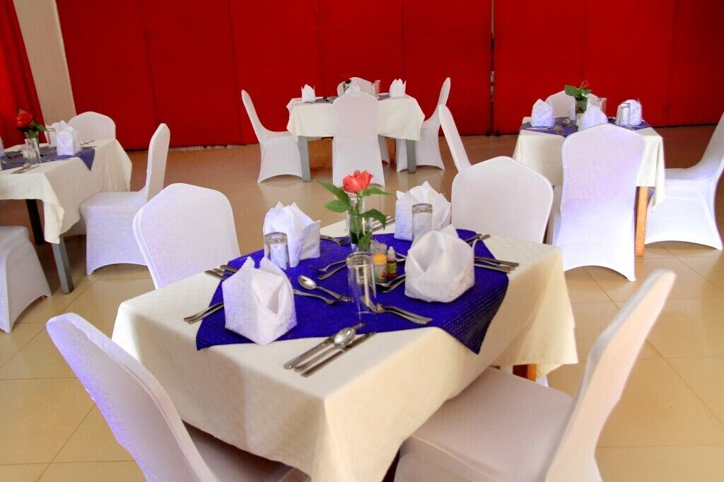 A banquet hall with round tables set for dining, white chairs, and red curtains in the background.