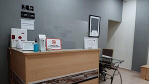 A reception desk with a sign indicating emergency contact information, a no-smoking sign, and a social distancing reminder. - CH Murallas II (Madrid)