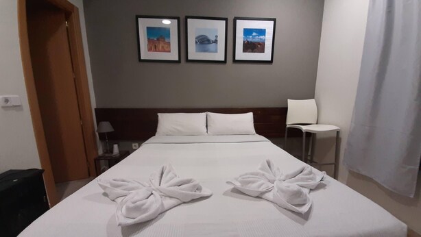 A hotel room with a large bed, two towels arranged on the bed, a nightstand with a lamp, a chair, and three framed pictures on the wall. - CH Murallas II (Madrid)