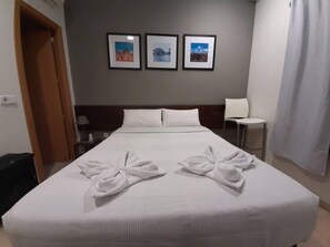 A hotel room with a large bed, two towels arranged on the bed, a nightstand with a lamp, a chair, and three framed pictures on the wall. - CH Murallas II  (Madrid)