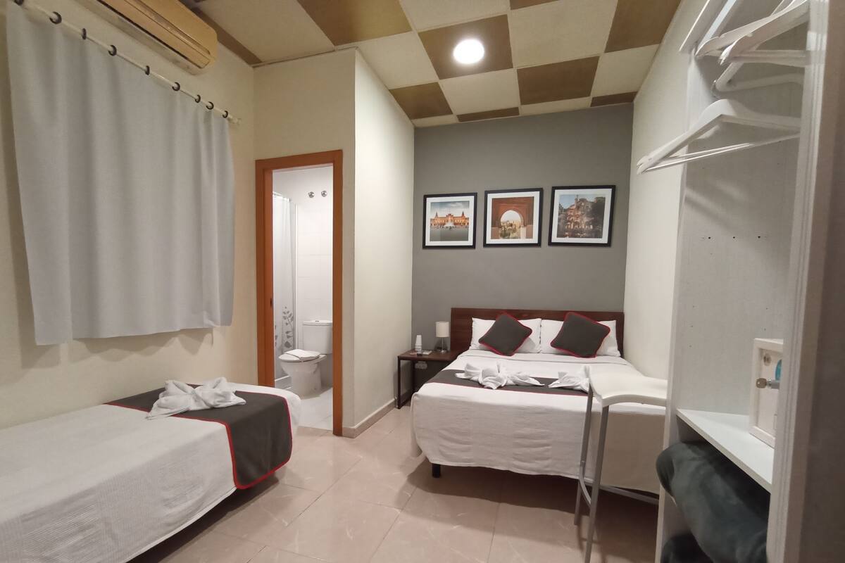 Habitación de hotel con dos camas, baño y una pequeña mesa con lámpara.