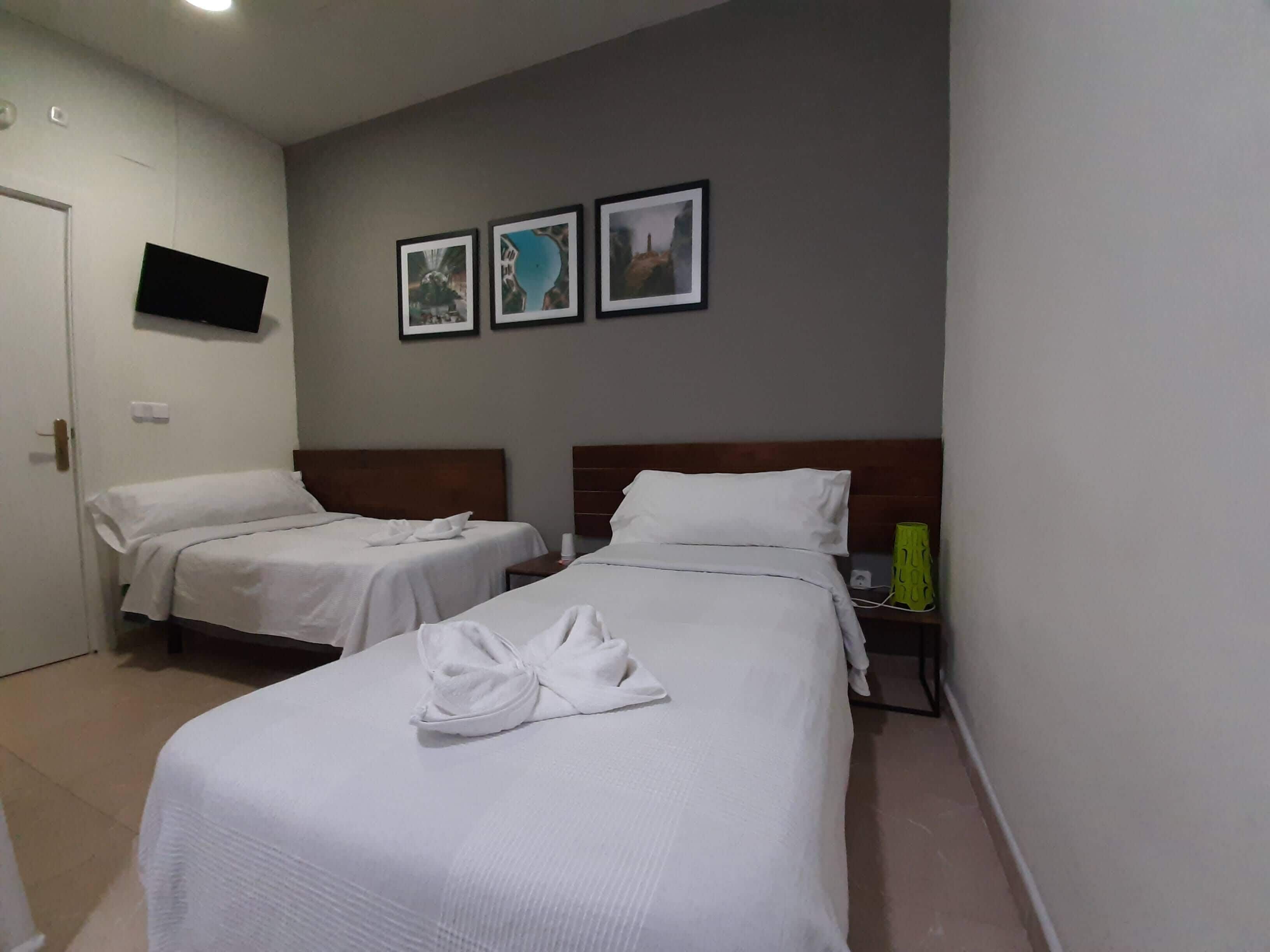 A hotel room with two beds, a flat-screen TV mounted on the wall, and three framed pictures above the beds.