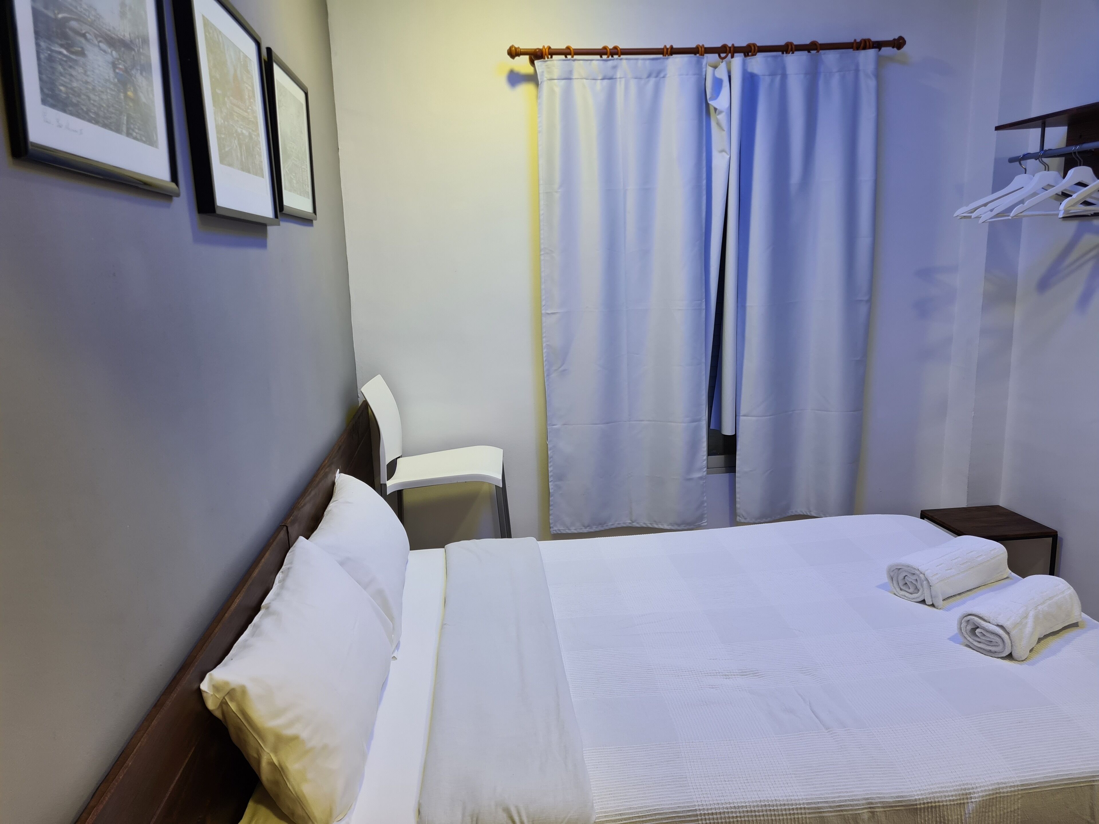 Una habitación de hotel con cama, una silla, una mesita pequeña y un armario con perchas.