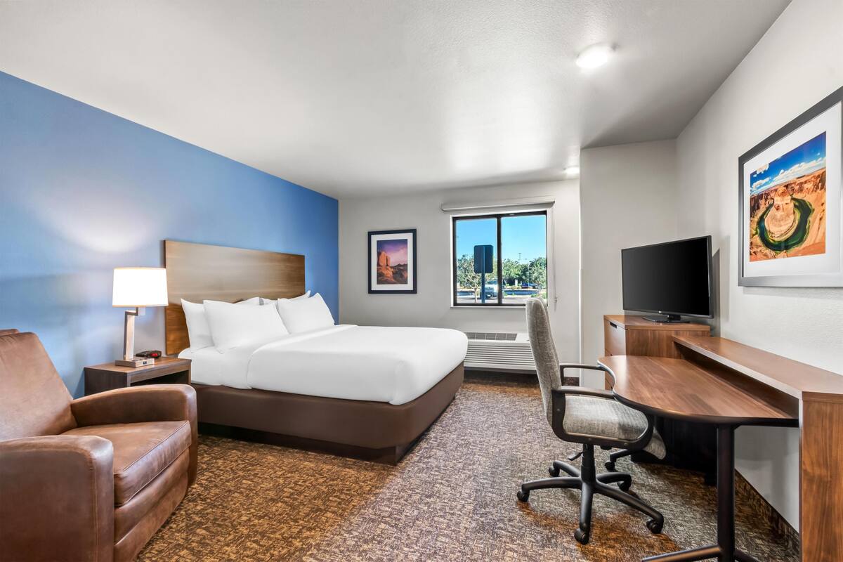 A hotel room with a bed, a desk, a chair, a TV, and a window with a view of the outdoors.