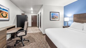 A hotel room with a bed, desk, chair, and a view of a cityscape through the window.