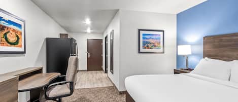 A hotel room with a bed, desk, chair, and a view of a cityscape through the window.