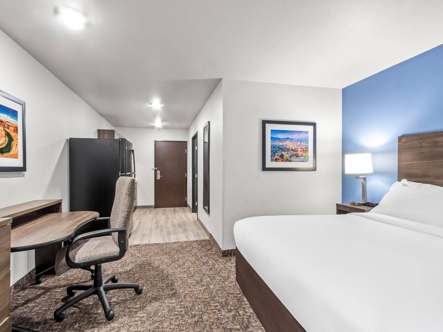 A hotel room with a bed, desk, chair, and a view of a cityscape through the window.