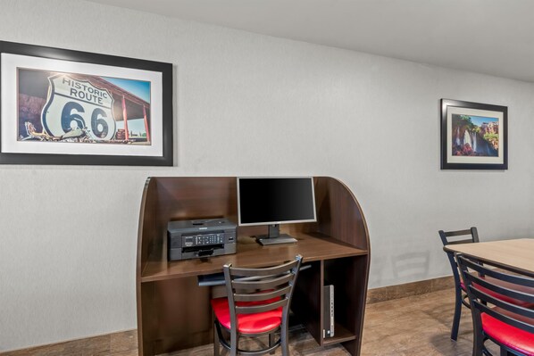 A room with a desk, a chair, a computer, a printer, and framed pictures on the wall.