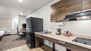 A modern kitchen with a black refrigerator, wooden cabinets, a countertop with a coffee maker, and a sink.