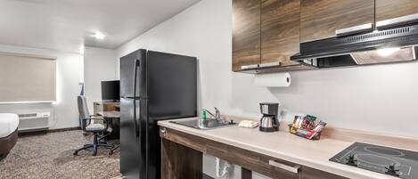 Une cuisine moderne avec un réfrigérateur noir, des armoires en bois, un plan de travail avec une machine à café et un évier.